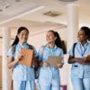 Three young women in scrubs walking through a hallway with textbooks